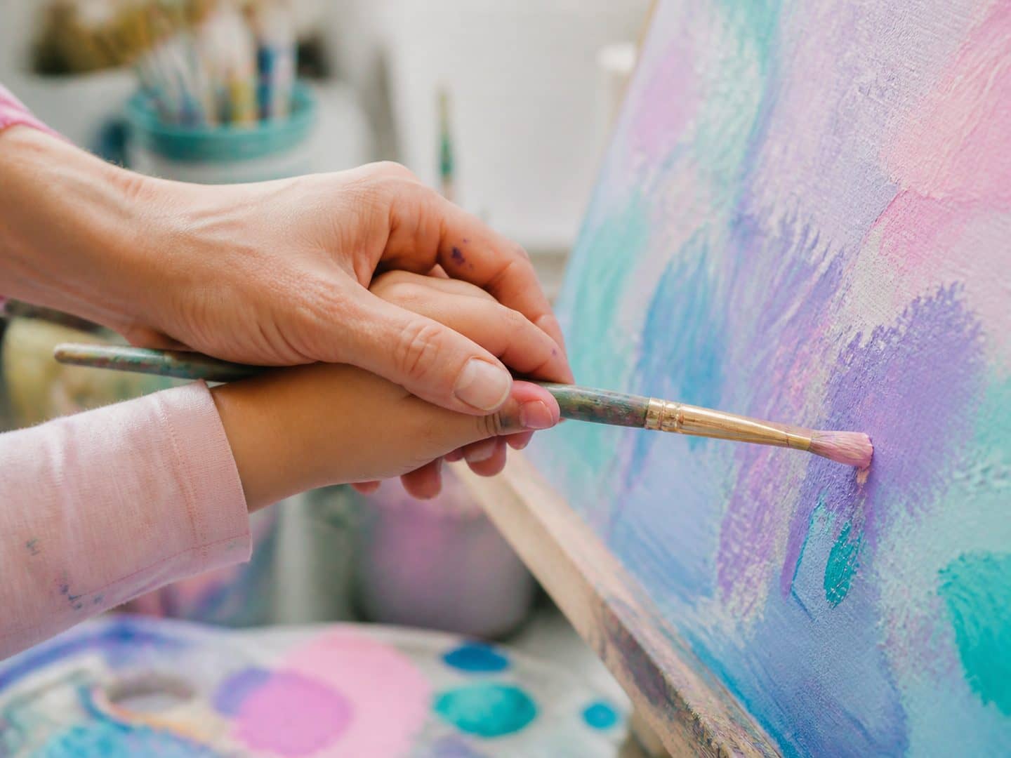 An instructor's hand guiding a child's hand with a paintbrush